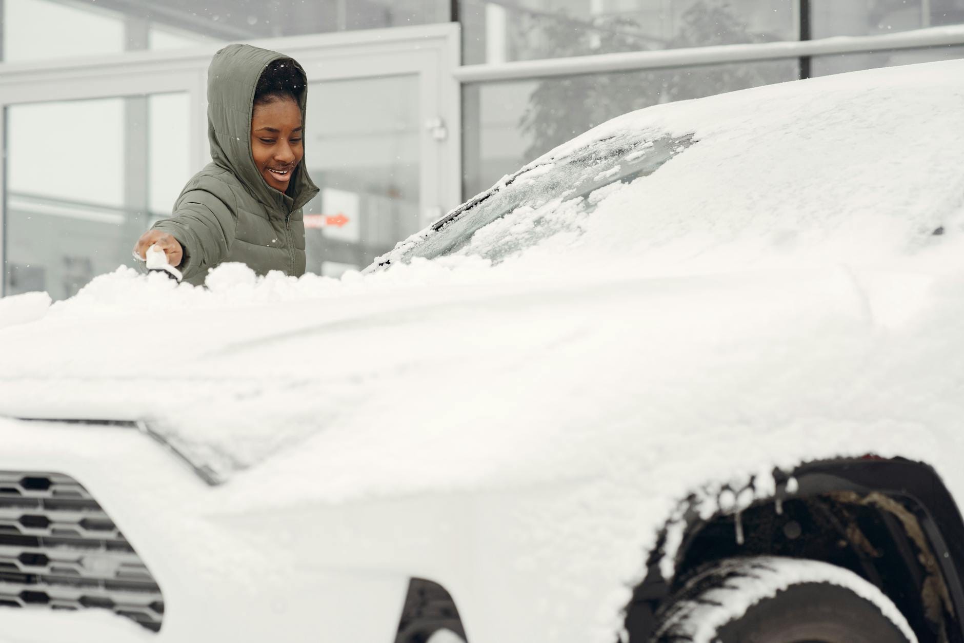 Kobieta w zielonej kurtce odśnieża auto zimą na zewnątrz