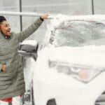 Kobieta w zimowym płaszczu odśnieża szybę samochodu