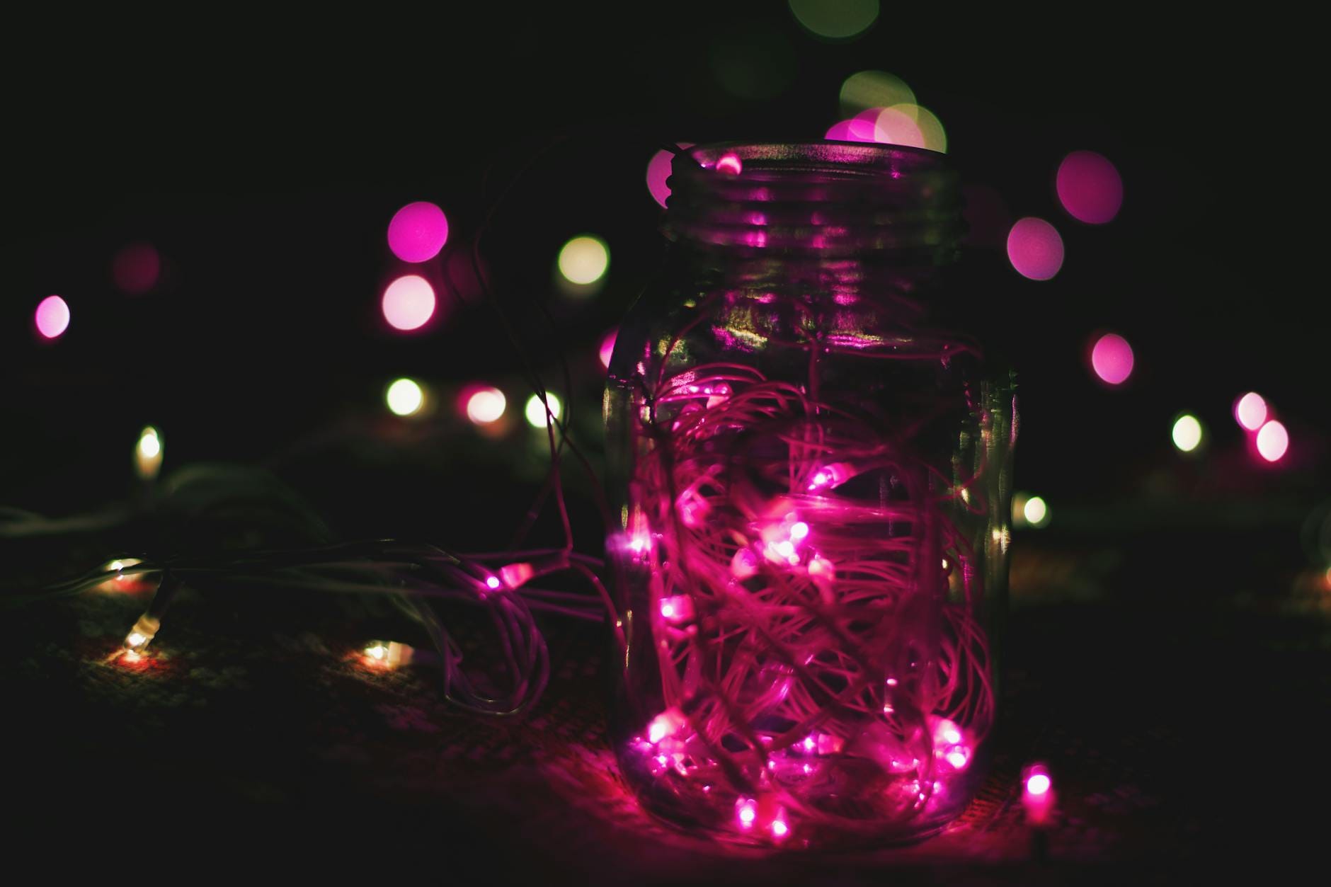 Słoik wypełniony różowymi lampkami LED na tle ciemnego bokeh